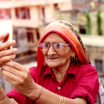 Old-senior-woman-taking-a-selfie-with-holding-smart-phone.png