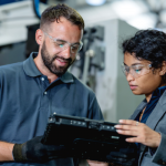 2_people_looking_at_at_table_in_a_manufacturing_setting.png