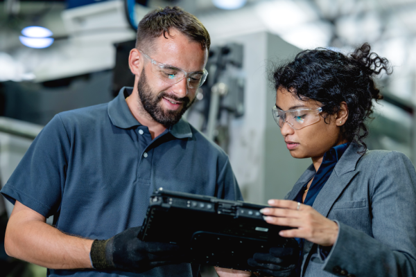 2_people_looking_at_at_table_in_a_manufacturing_setting.png